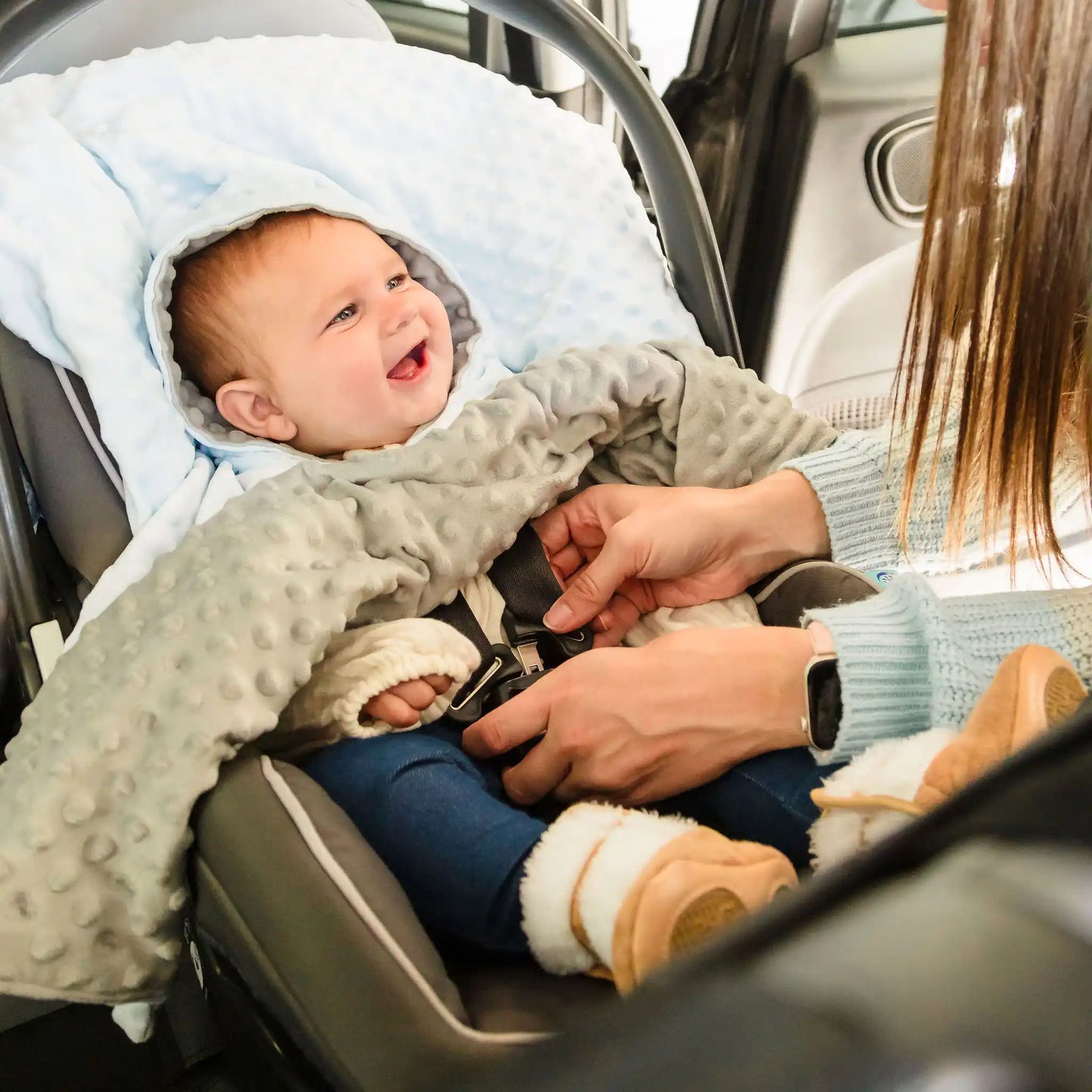 Car seat poncho on baby boy in car seat with mom buckling the straps - blue